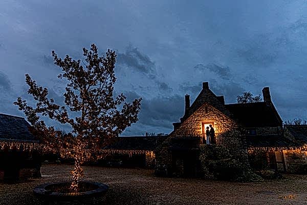 Twilight over cozy stone cottage with festive lights.