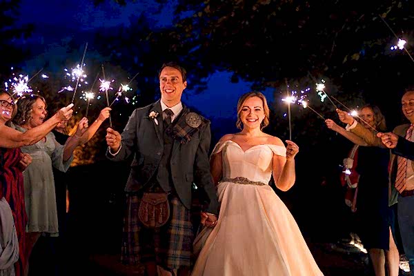 Bride, groom, guests with sparklers at twilight wedding.
