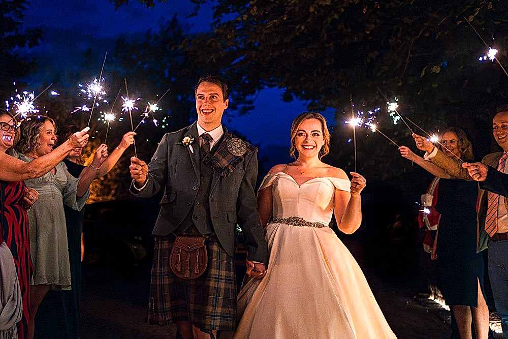 Bride and groom holding sparklers at evening wedding.