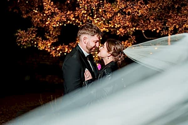 Couple embracing at night under illuminated tree.