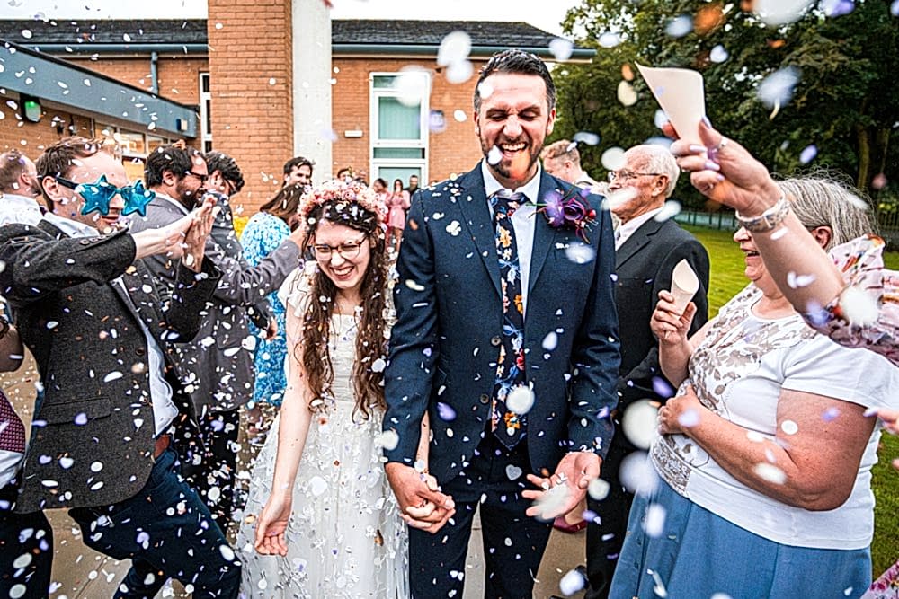 Joyful wedding couple with guests throwing confetti.