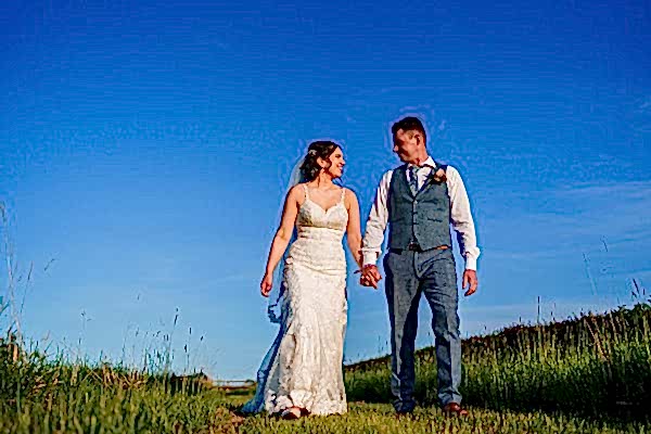 Bride and groom walking together in sunny countryside.