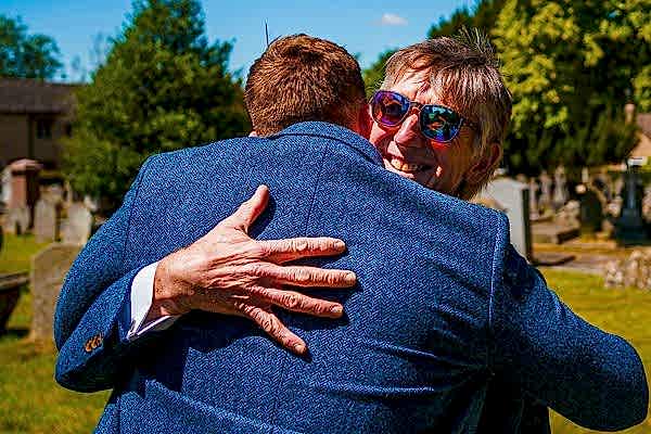 Embracing people smiling outdoors on a sunny day.