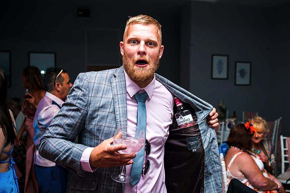 Man with surprised look holding drink and hiding bottle.