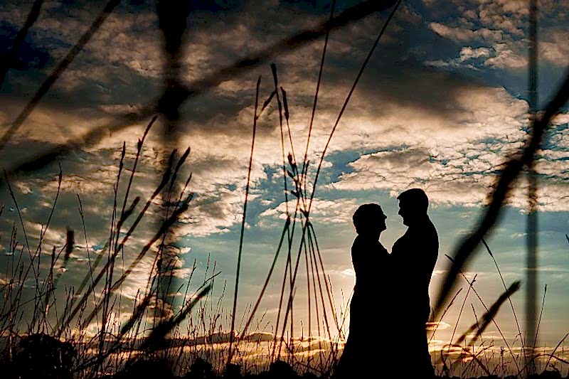 Couple silhouette against sunset sky in field.