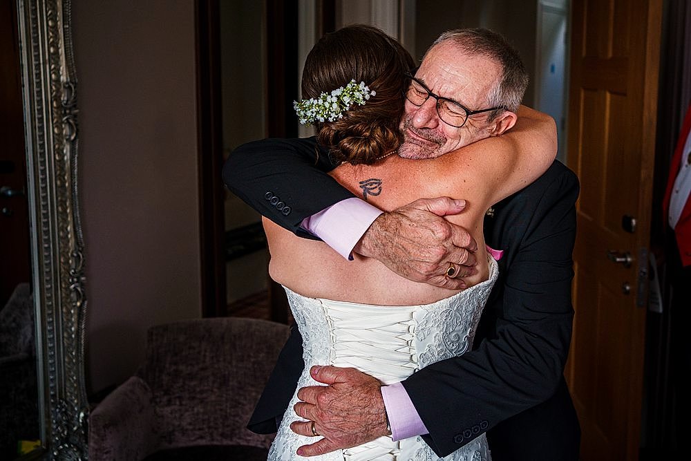 Emotional wedding hug with smiling elder man and bride.