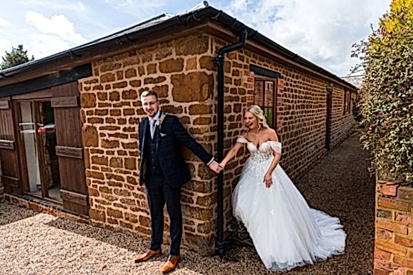 Bride and groom holding hands by stone building.