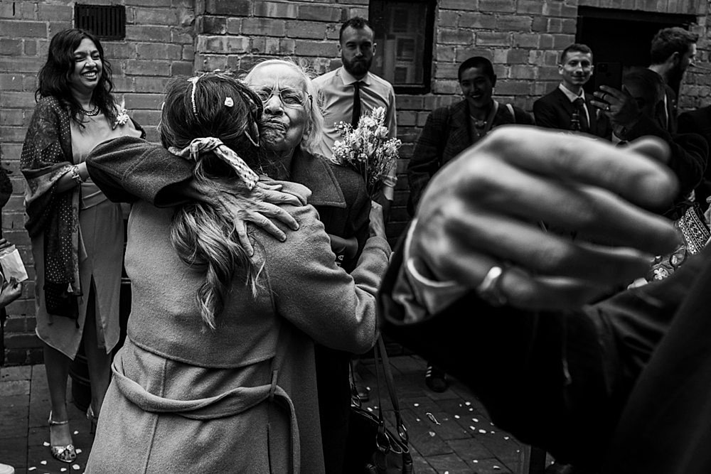 Emotional wedding hug with smiling guests in background.