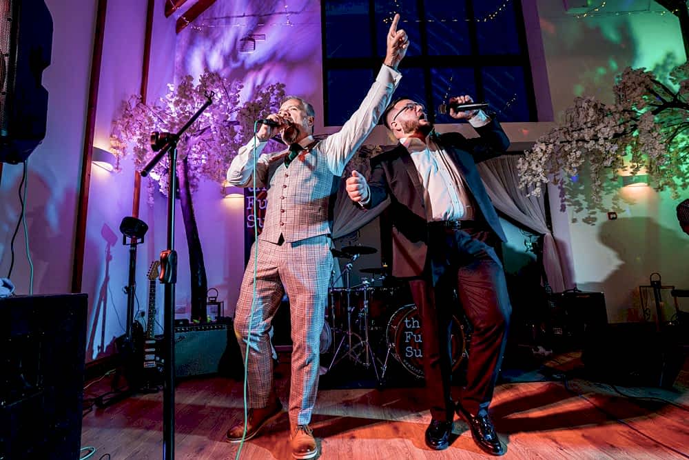 Two singers performing energetically on stage at an event.