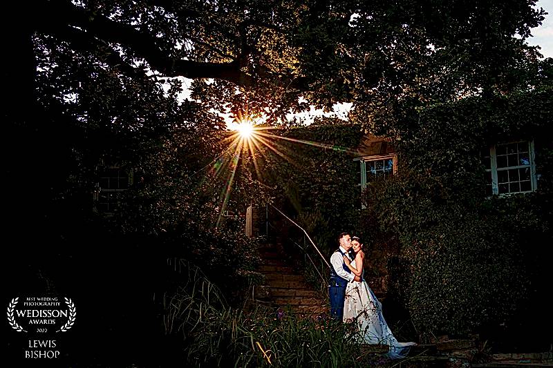 Couple kissing at sunset by ivy-covered house.