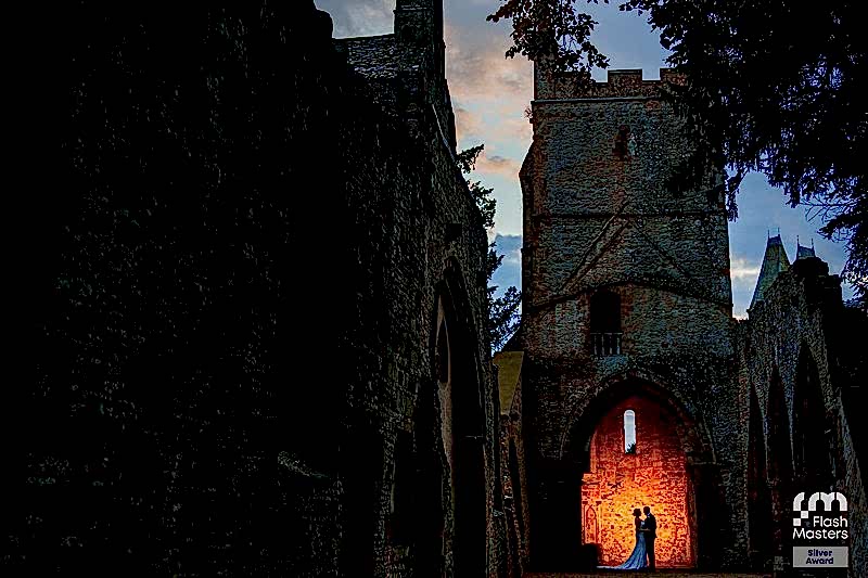 Couple embracing in illuminated archway of historic ruins at dusk.