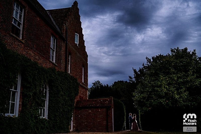 Couple embracing by historic brick building at dusk.