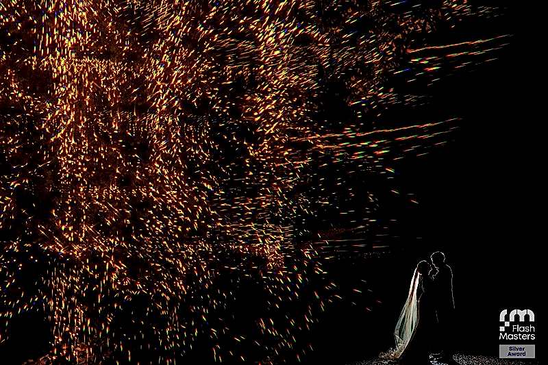 Couple silhouetted against sparkling fireworks display.