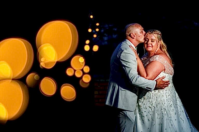 Couple embracing at night with warm bokeh lights.