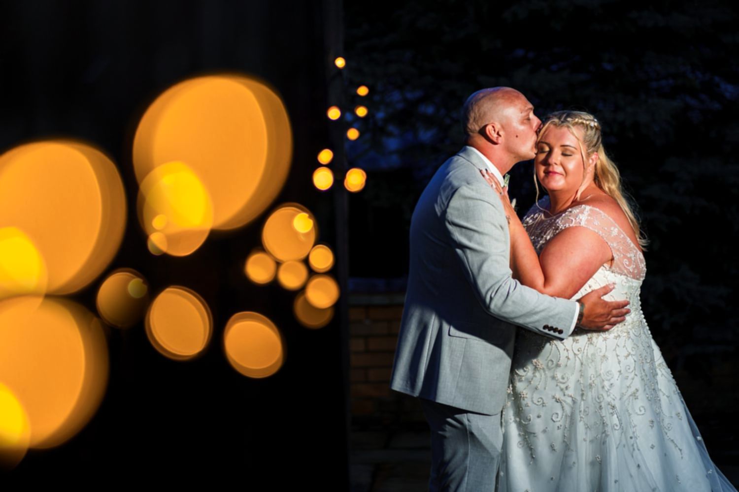 Couple embracing at night with warm bokeh lights.