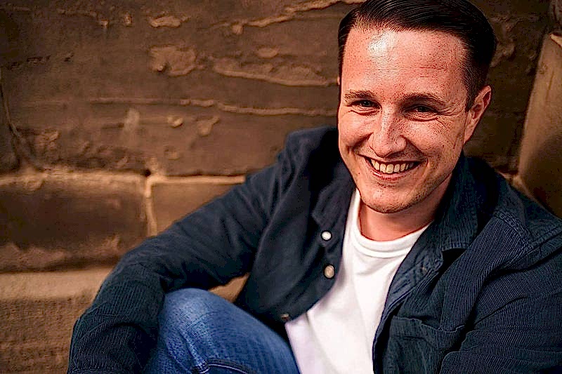 Man smiling sitting against brick wall.