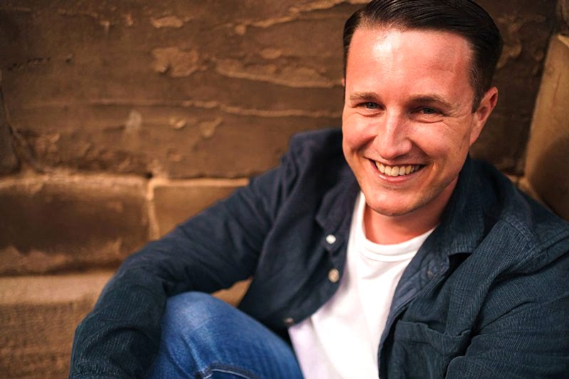 Smiling man sitting against brick wall.