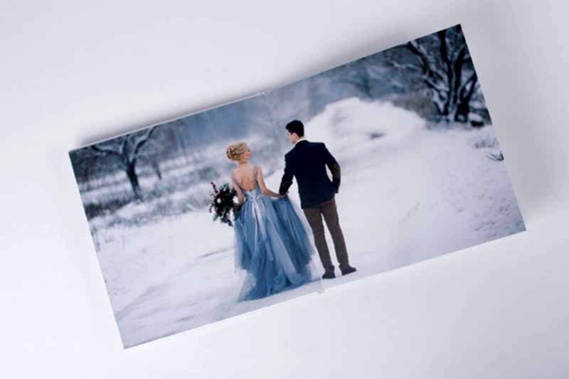 Couple in winter wedding attire walking on snowy path.