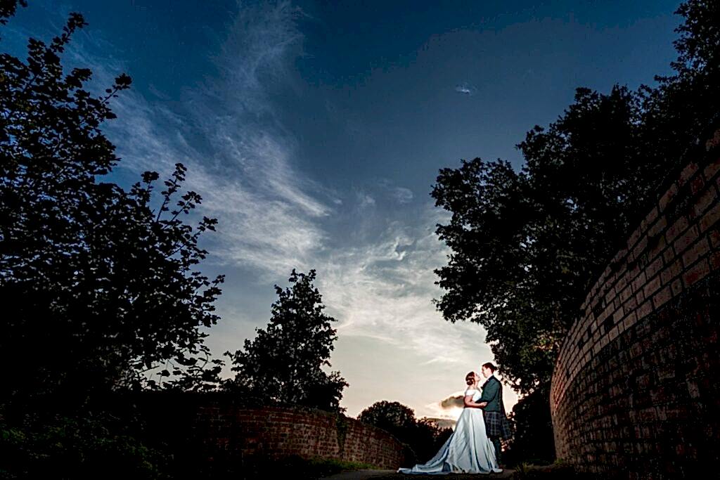 Couple in wedding attire at dusk under dramatic sky.