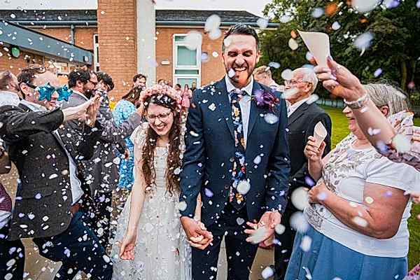 Bride and groom enjoying confetti shower at wedding.