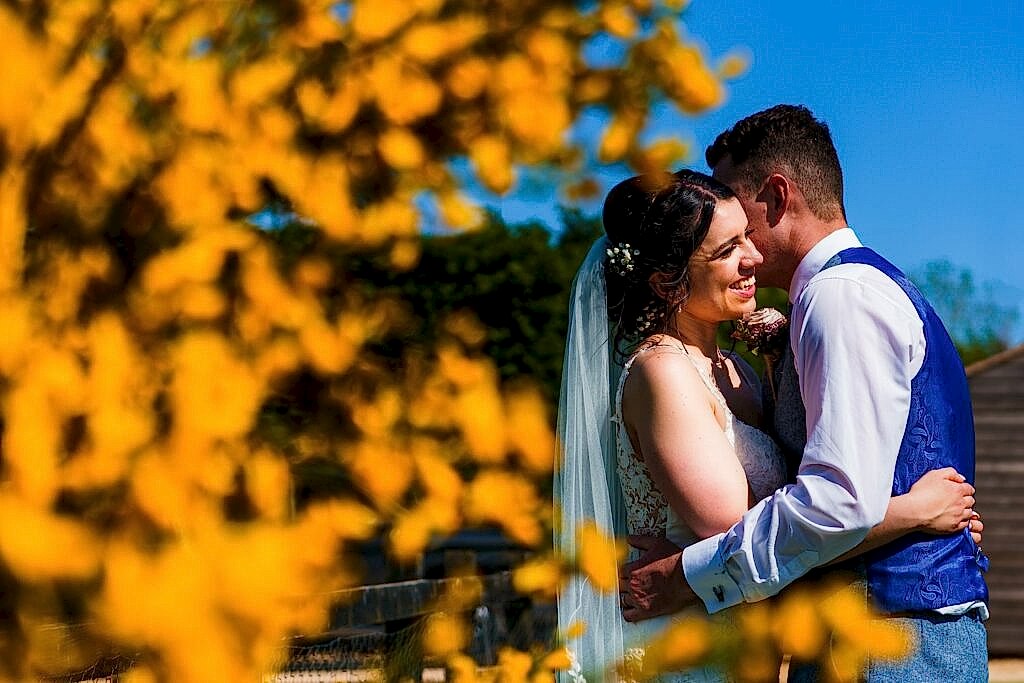 Bride and groom embracing on sunny day with flowers
