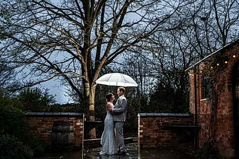 Couple with umbrella in romantic rainy wedding scene.
