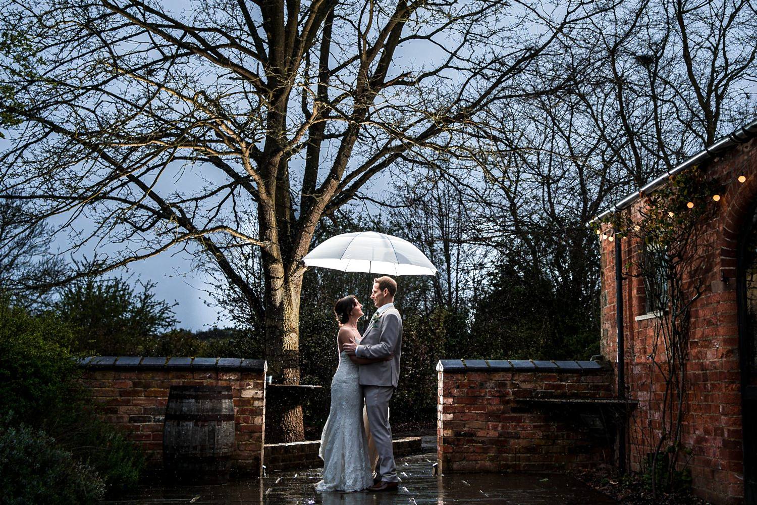 Couple with umbrella in romantic rainy wedding scene.