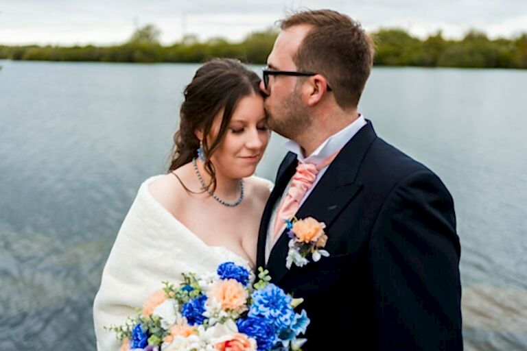 Bride and groom by the lake, wedding flowers present.