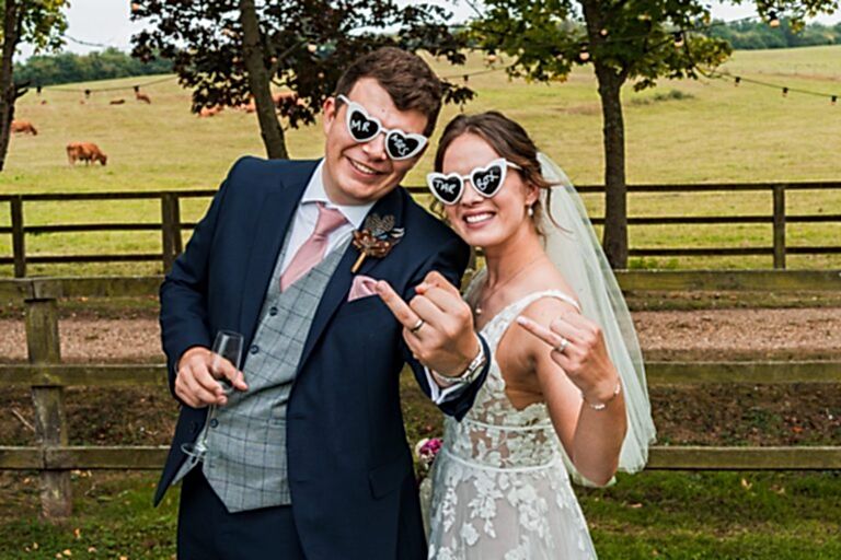 Bride and groom with heart-shaped glasses outdoors.