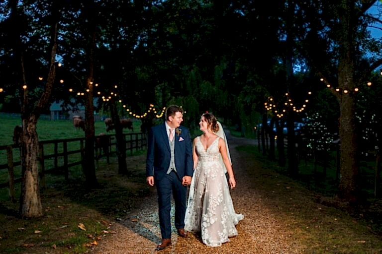 Bride and groom walking under fairy lights.