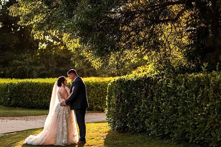 Couple embracing in sunlit garden setting.