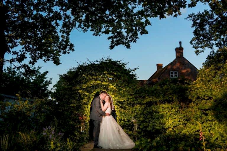 Bride and groom kiss under garden archway.