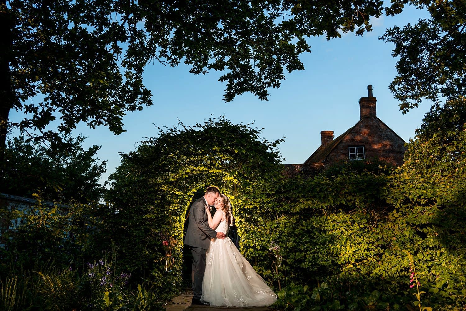 Bride and groom kiss under garden archway.