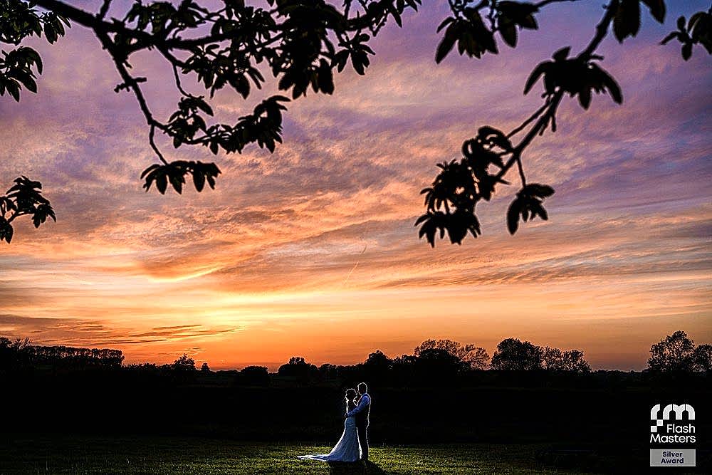 Bride and groom at sunset under tree branches.