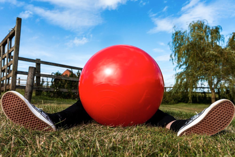 Person hidden behind large red ball outdoors.