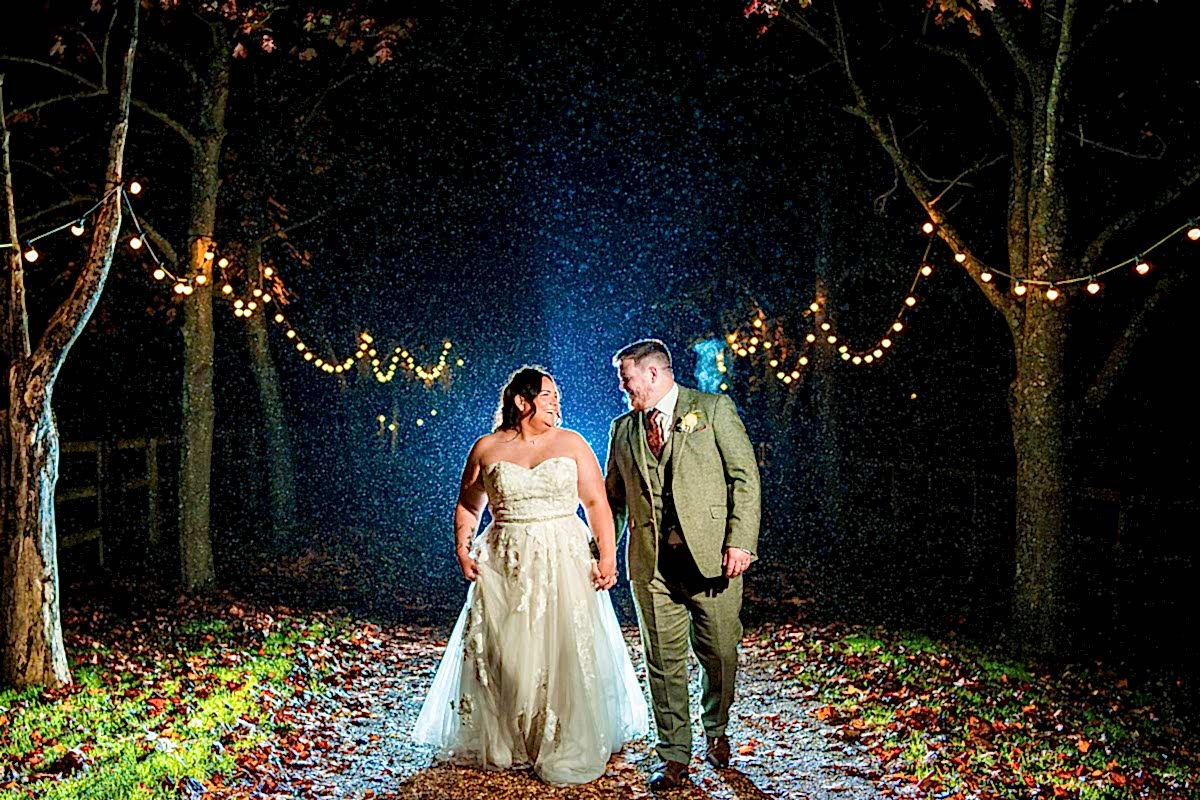 Bride and groom walking under string lights in rain.