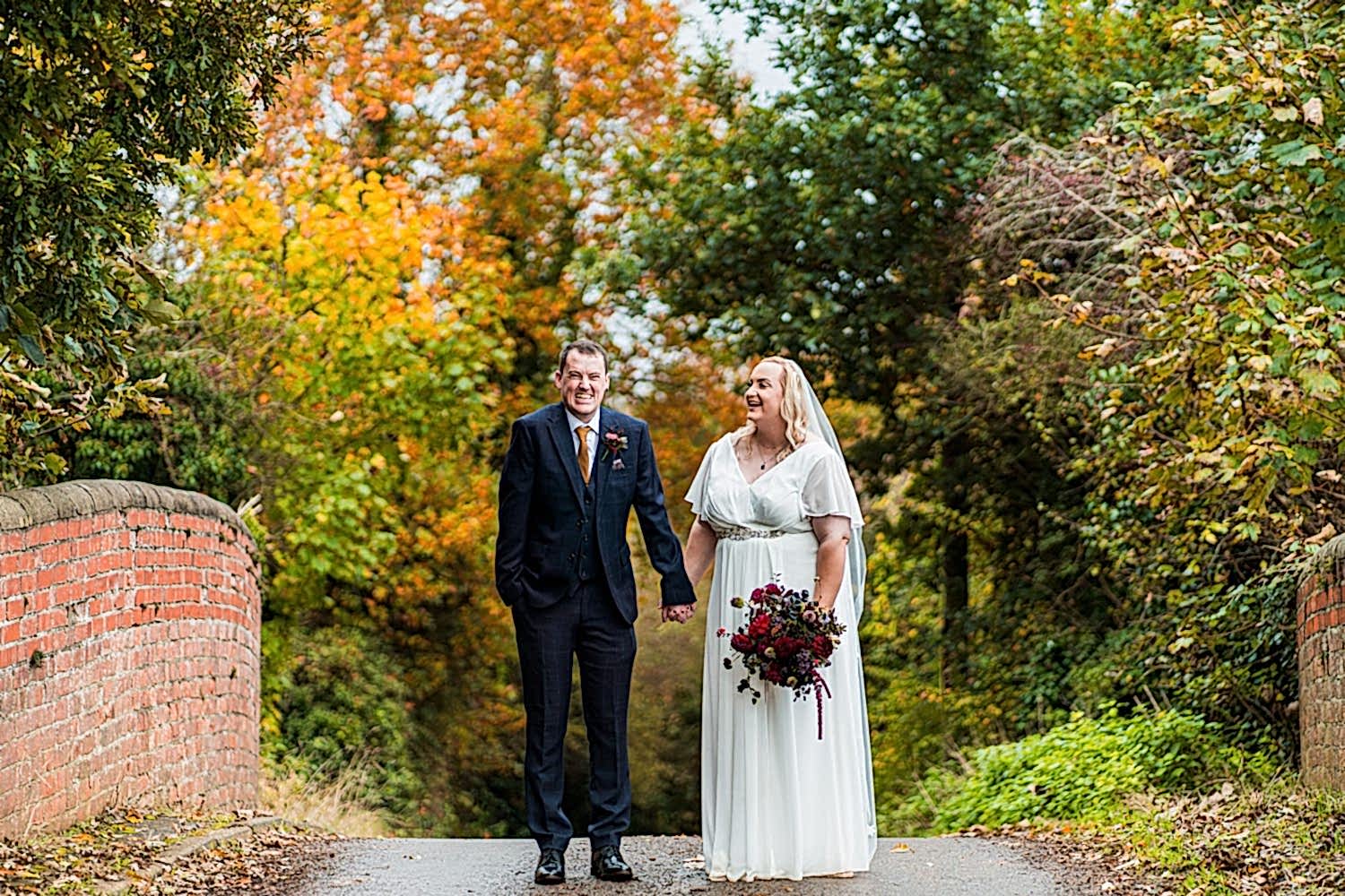 Bride and groom on autumnal bridge.