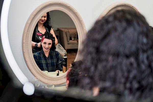Hairdresser styling woman's hair in salon mirror.