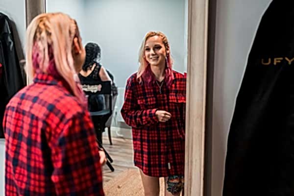 Woman smiling at reflection in mirror, wearing plaid shirt.