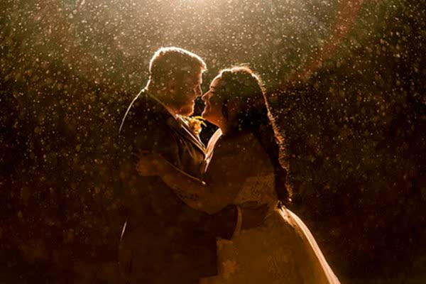 Couple embracing in rain under dramatic light.