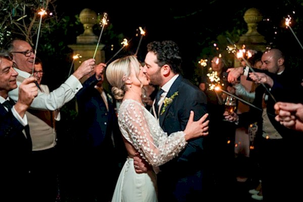 Newlyweds kiss surrounded by sparklers at night.