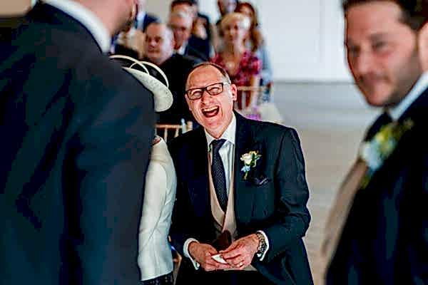 Man laughing at wedding ceremony, guests seated