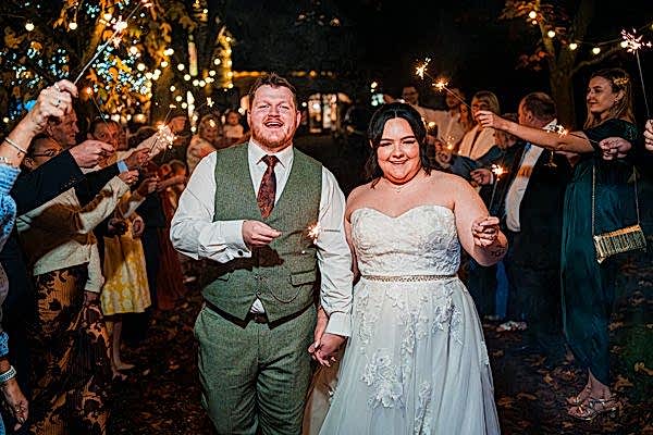 Couple walks with sparklers at wedding celebration.