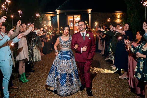 Couple walking through sparkler-lit celebration at night.