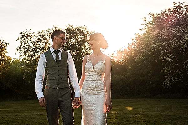 Bride and groom holding hands outdoors at sunset.