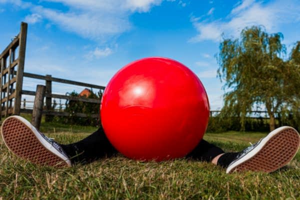 Person hidden behind large red ball in field.