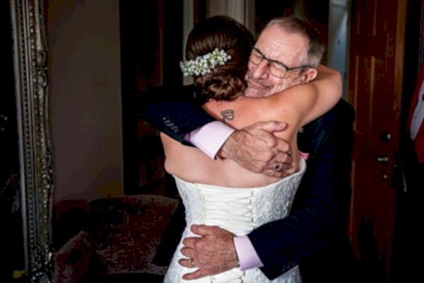 Bride embraces elderly man warmly, emotional moment.