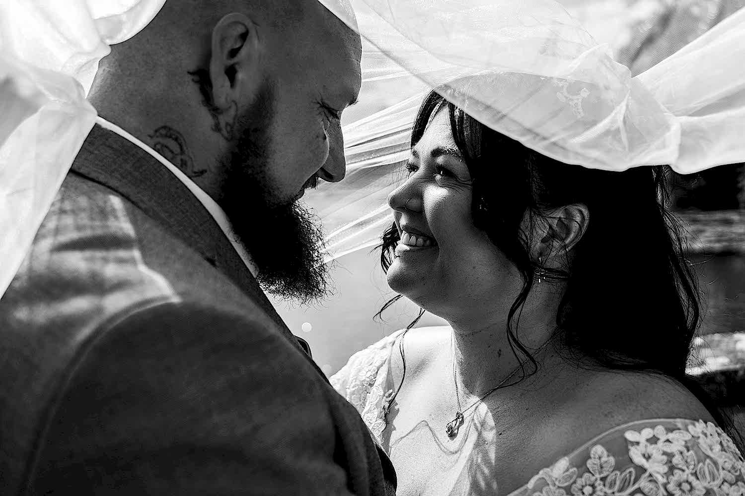 Bride and groom smiling under wedding veil.