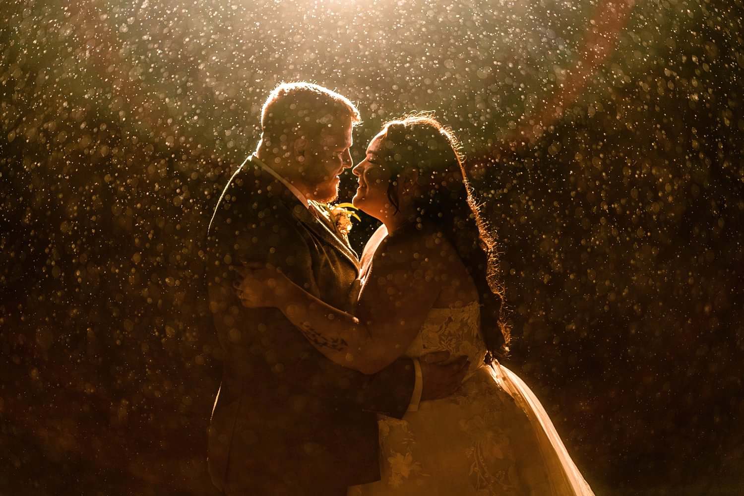 Couple embraces in rain under glowing light.