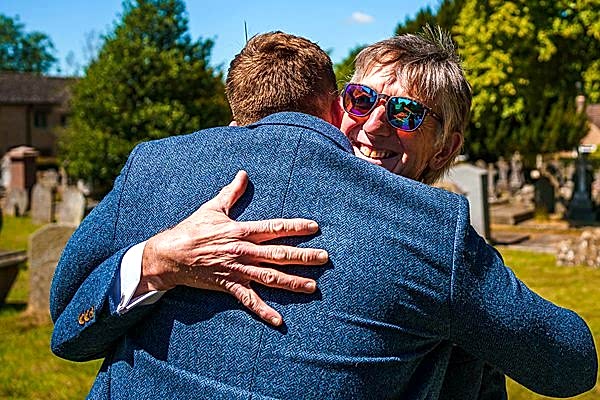 Two people embracing in a sunny cemetery.